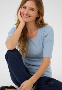 Lichtblauw geribbeld T-shirt met korte mouwen. Draagt met donkerblauwe jeans. Soepele textuur, aansluitend ontwerp met een ronde hals.