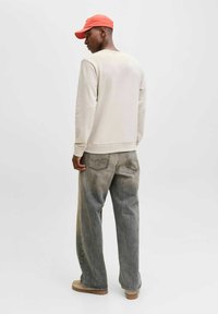 Sweat-shirt crème avec ourlet côtelé, jean gris à jambes larges, et casquette de baseball rouge, vus de dos sur un fond uni.