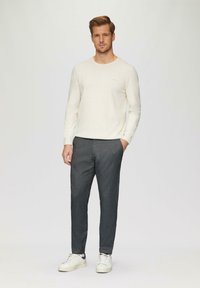 Lichtbeige gebreide trui met ronde halslijn, gecombineerd met donkergrijze geprinte broeken en witte sneakers. De trui heeft een subtiele merkdetails.