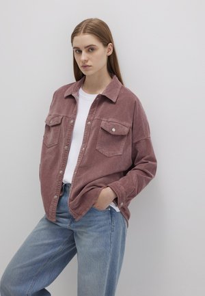 Kariertes Hemd in staubrosa mit zwei Brusttaschen, Knopfleiste und Kragen, kombiniert mit hellblauen Jeans.