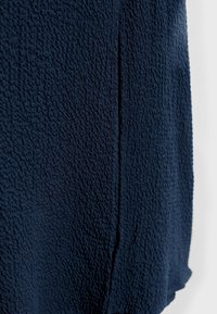Tissu texturé bleu foncé avec un subtil détail de pli vertical sur un fond lisse et plus clair.