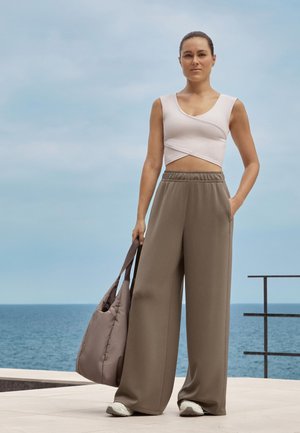 White cropped top with a twisted design, paired with loose, olive-green trousers. Features a soft, textured fabric and gray shoulder bag.