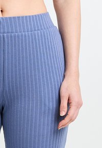 Des pantalons bleus à taille haute côtelés qui présentent un matériau texturé avec des rayures verticales, mettant en avant une silhouette ajustée et une taille sans couture.