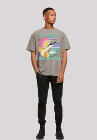 Graues Baumwoll-T-Shirt mit einem Frontaufdruck, der einen Regenbogen, eine Ozeanszene und den Text "PINK FLOYD" zeigt. Kombiniert mit schwarzen Sweatpants und Turnschuhen.
