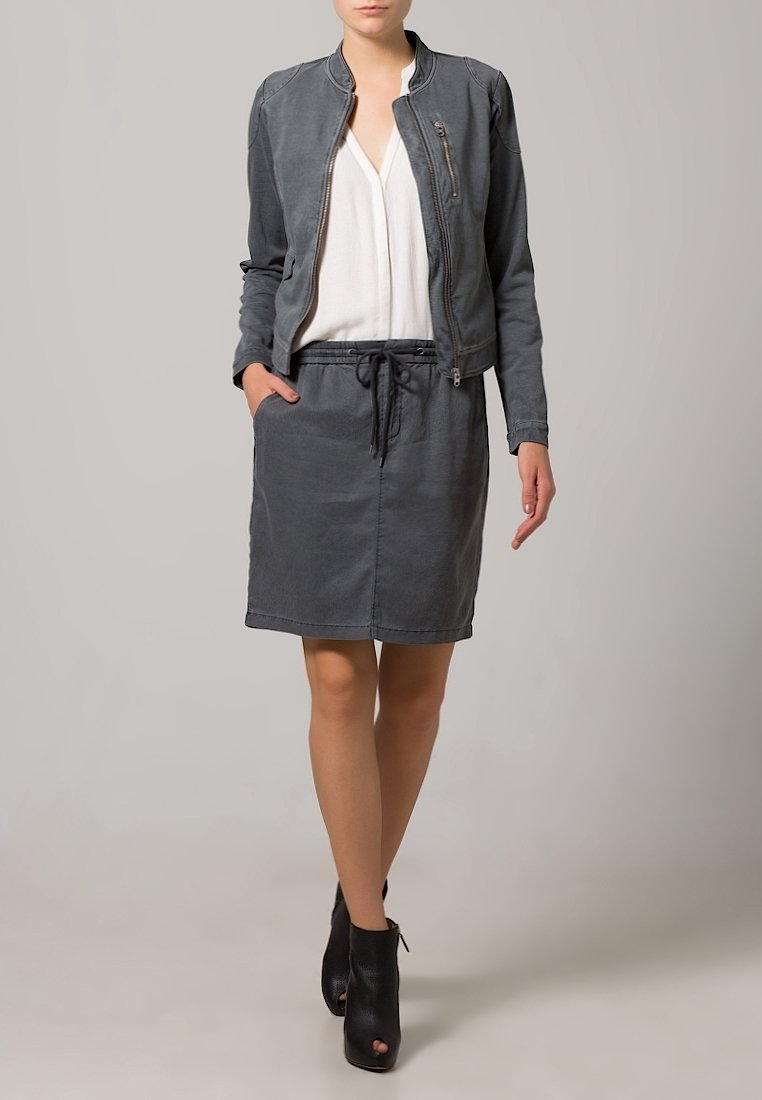 Chaqueta bomber de cuero gris sobre una blusa blanca, combinada con una falda gris a juego. El conjunto incluye una cintura con cordón y botines hasta el tobillo.