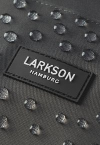 Black fabric with raised droplets, featuring a textured surface. A rectangular black label displays "LARKSON HAMBURG" in white letters.