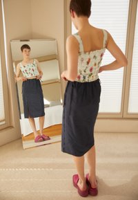 Top cropped com estampado floral e alças largas, saia azul-marinho com fenda lateral e sandálias plataforma rosa, refletidos num espelho de corpo inteiro.