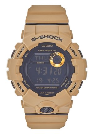 Montre digitale Casio G-Shock couleur beige avec podomètre, Bluetooth, étanche, boutons étiquetés et cadran rond avec accents noirs et dorés.