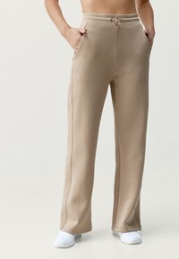 Lichtbeige joggerbroeken met een drawstring taille, zijzakken en een gladde textuur. Licht uitlopende uitstraling met witte schoeisel.