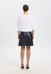 Haut blanc oversize avec manches tombantes, assorti à une jupe noire en cuir ajustée. Textures lisses, design minimaliste, et talons à bride à la cheville.