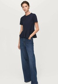 Top peplum blu navy realizzato in tessuto morbido con maniche corte, abbinato a jeans azzurri a vita alta e gamba ampia, che mostrano uno stile casual.