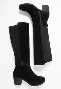 Stivali neri al ginocchio in finitura suede, con zip laterale e dettaglio fibbia sopra la caviglia. Tacco a blocco con superficie testurizzata.