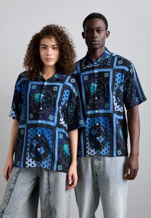 Chemises bleues à manches courtes avec des motifs géométriques et circulaires élaborés. Fabriquées en tissu à surface texturée et avec des boutons sur le devant.