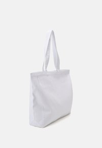Sac en coton blanc avec deux poignées supérieures, de forme rectangulaire et au design minimaliste. Le tissu a une texture lisse et mate.