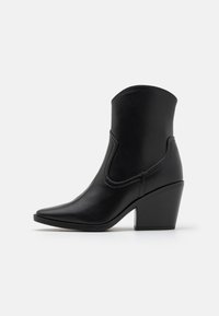 Botas negras hasta el tobillo con punta afilada, un tacón romano medio y una textura suave similar al cuero, con detalles recortados en los lados.