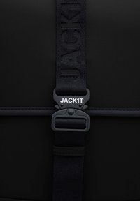 Zaino nero dal design elegante, con una spessa tracolla testurizzata etichettata "JACK1T" e una fibbia in plastica resistente di colore nero opaco.