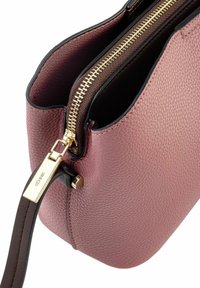 Różowa torba skórzana o teksturowanej powierzchni z złotym zamkiem błyskawicznym, brązowym wnętrzem i odpinanym brązowym paskiem. Posiada okrągły kształt i gładkie wykończenie.