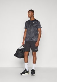 Svart treningstrøye med teksturert mønster, sammen med svarte shorts med en logo. Tilbehør inkluderer en svart treningsbag og joggesko.