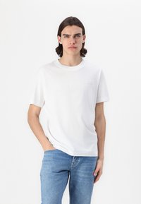 Hvit bomulls T-skjorte med rund hals, korte ermer og en subtil logo på brystet. Kombinert med blå denimjeans.