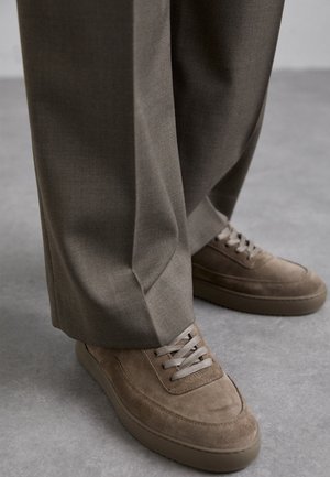 Barna velúr sportcipők texturált részletekkel és világosszürke fűzőkkel, lazán illeszkedő, világosbarna nadrággal, sima anyagból.