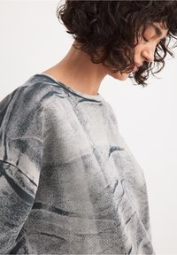 Sudadera gris con patrón y corte holgado, con cuello redondo y superficie texturizada, que muestra diseños abstractos en tonos oscuros y claros.