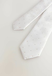 Corbata blanca texturizada con pequeños puntos beige uniformemente espaciados, extendida sobre una superficie clara.