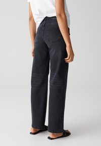 Black wide-leg jeans with a high waist, featuring double back pockets and a clean finish. Worn with black slide sandals on a neutral background.