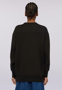 Svart oversized sweatshirt med rundad halsringning, sänkta axlar, ribbstickade muddar och nederkant, tillverkad av mjukt tyg. Enfärgad textur, inga mönster.