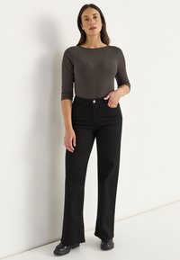 Zwarte jeans met een rechte pijp en een aansluitend donkergrijs langemouwen ribbeldtop. De outfit heeft minimale hardware.