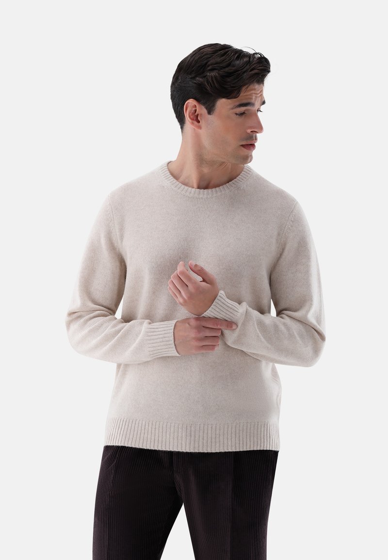 Maglione beige a collo rotondo in un morbido knit, con polsini e orlo a coste, abbinato a pantaloni in velluto a coste scuri. Vestibilità sartoriale con una superficie liscia.