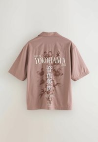 Majica kratkih rukava ružičaste boje s ležernim krojem. Sadrži tiskane cvjetne uzorke i natpis "YOKOHAMA" na leđima. Pamuk.