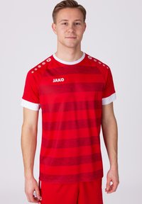 Rotes Sportshirt mit horizontalen Streifen, weißen Akzenten am Kragen und an den Ärmeln sowie dem Logo "JAKO" auf der Vorderseite. Mit abgesetzten Schulterpunkten.