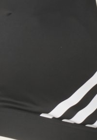 Sujetador deportivo negro con textura suave, que presenta tres rayas diagonales blancas en el lado izquierdo y un diseño sin costuras.