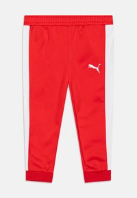 Pantalons de sport rouges avec des panneaux latéraux blancs et une taille élastique, comportant un petit logo blanc à l'avant. Texture lisse, coupe ajustée.