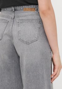 Šedé džíny z denimu s vysokým pasem, rovnými nohavicemi a dvěma zadními kapsami. Na zadním pásu je přišitá hnědá kožená nášivka s logem značky.