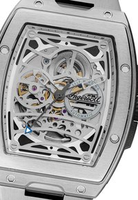 Zilveren skeleton horloge met een rechthoekige kast, intrigerende tandwieldetails, blauwe accenten op de secondewijzer en een transparante wijzerplaat die de beweging toont.