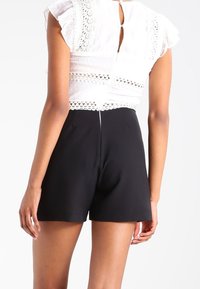 Haut blanc avec détails en dentelle et bas noirs courts. Le haut présente des manches à volants et une petite ouverture en trou de serrure dans le dos. Texture lisse dans l'ensemble.