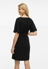 Svart knälång klänning med åtsittande midja, korta ärmar och textil med små utskärningar.