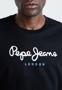 Camiseta negra de algodón con el logotipo en cursiva blanco de "Pepe Jeans" y el texto azul "LONDON". Cuello redondo y textura suave.