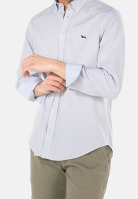 Hellblau-weiß gestreiftes Hemd mit Knöpfen, aus Baumwollmaterial, mit einem kleinen gestickten Logo auf der Brust und hochgekrempelten Ärmeln.