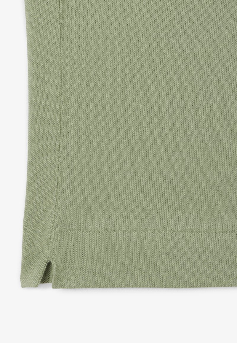 Light green knitted fabric with a textured surface, featuring side slits at the hem for flexibility and a clean finish along the edges.