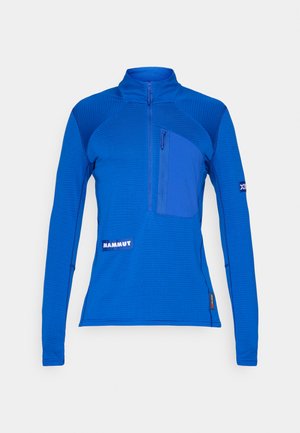 Blue long-sleeve pullover made of textured fabric, featuring a zippered chest pocket, a logo patch, and contrasting panel details.