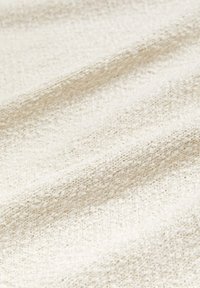 Tissu texturé de couleur crème avec une surface légèrement côtelée ; présente de petits motifs tissés, créant une apparence douce et chaleureuse.