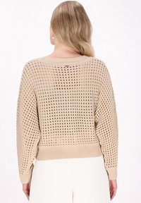 Maglione lavorato a maglia beige con un motivo aperto e testurizzato. Presenta un collo rotondo e maniche lunghe, con polsini e orlo a coste.