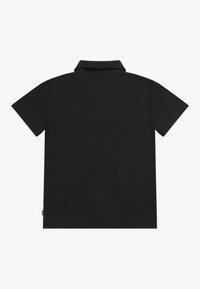 Polo noir à manches courtes posé à plat, montrant le dos avec un col et une petite étiquette rouge sur la couture latérale gauche.