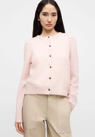 Ροζ πλεκτή ζακέτα με στρογγυλή λαιμόκοψη, κουμπώνει μπροστά με κουμπιά και έχει ριμπ τελείωμα. Διαθέτει σκούρα κουμπιά και απαλό, υφασμάτινο υλικό με υφή.