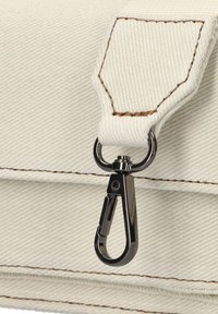Canvas tasriem met bevestiging van een zilveren metalen clip. De stof is crème kleurig met bruine stiksels en een gestructureerde afwerking.