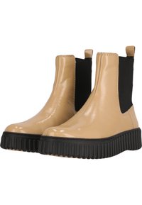 Bottines Chelsea en vernis beige avec panneaux latéraux élastiques et semelle en caoutchouc noir. Texture lisse et design à bout rond.