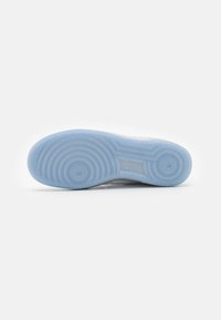 Suola di sneaker con suola in gomma azzurro chiaro, caratterizzata da motivi circolari e ondulati del battistrada. Texture liscia, branding minimale visibile.