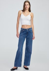 Biały dziergany top krótki na ramionach, połączony z szerokimi niebieskimi dżinsami. Dżinsy mają klasyczny pięcio-kieszeniowy krój i średnie wykończenie w talii.